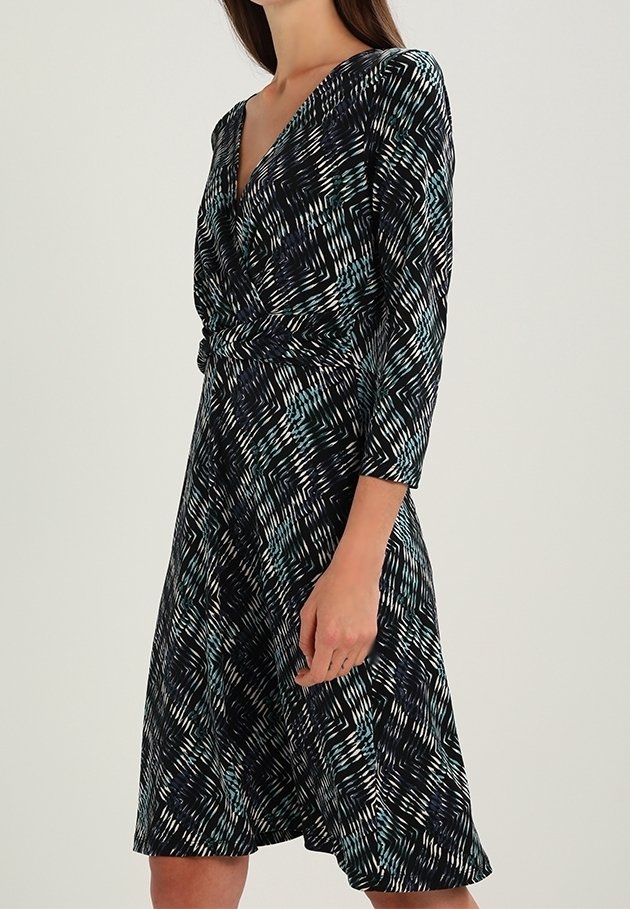 Knä-lång klänning i marinblått med ett geometriskt mönster i turkos och vitt. Har en V-ringning och trekvartsärmar, tillverkad av mjuk tyg.