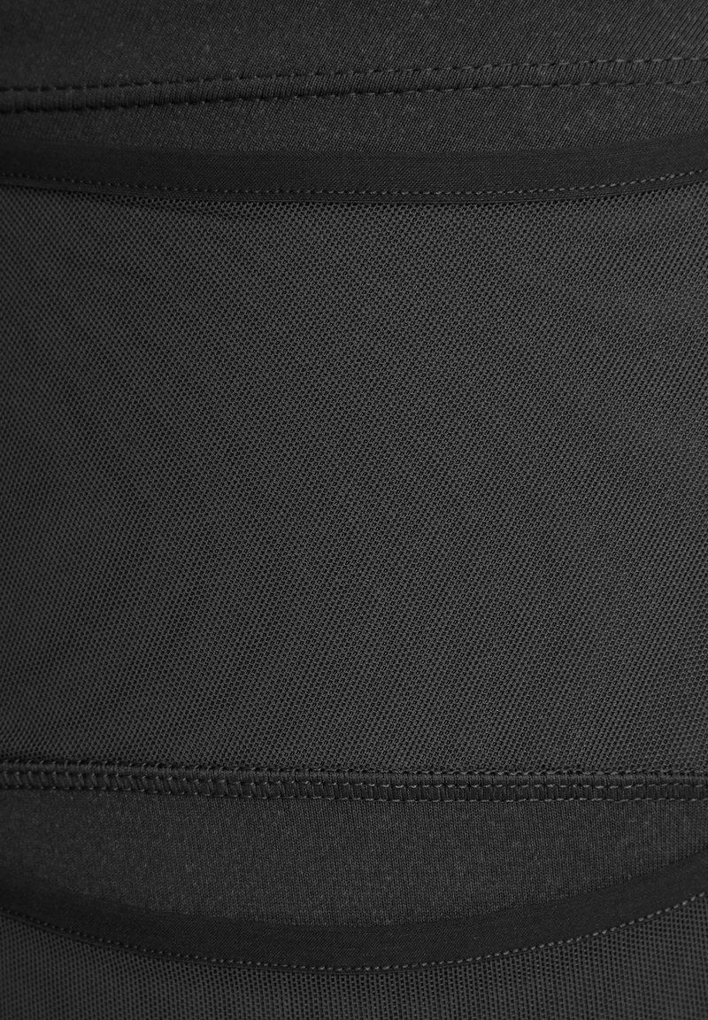 Tela negra con un patrón texturizado, que presenta secciones lisas y líneas de costura en contraste. El material parece elástico y se ajusta al cuerpo.