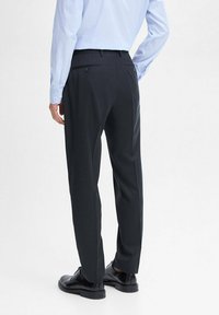 Black tailored trousers with a smooth texture, featuring two back pockets and subtle crease details, paired with black shoes.