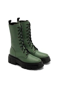 Bottes de combat en cuir vert avec lacets noirs, tige haute, finition texturée et semelle noire épaisse. Dotées de languettes de traction sur les côtés.
