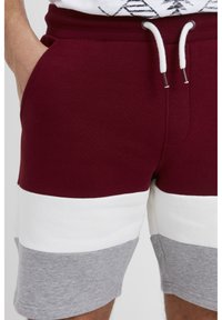 Maronfarvede og grå bomuldsshorts med hvide vandrette striber, der har en elastisk talje og snor. Inkluderer sidelommer.