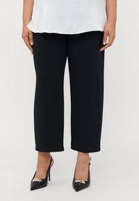 Black wide-leg pants made of a smooth fabric, paired with black high-heeled shoes featuring a gold accent on the toe.