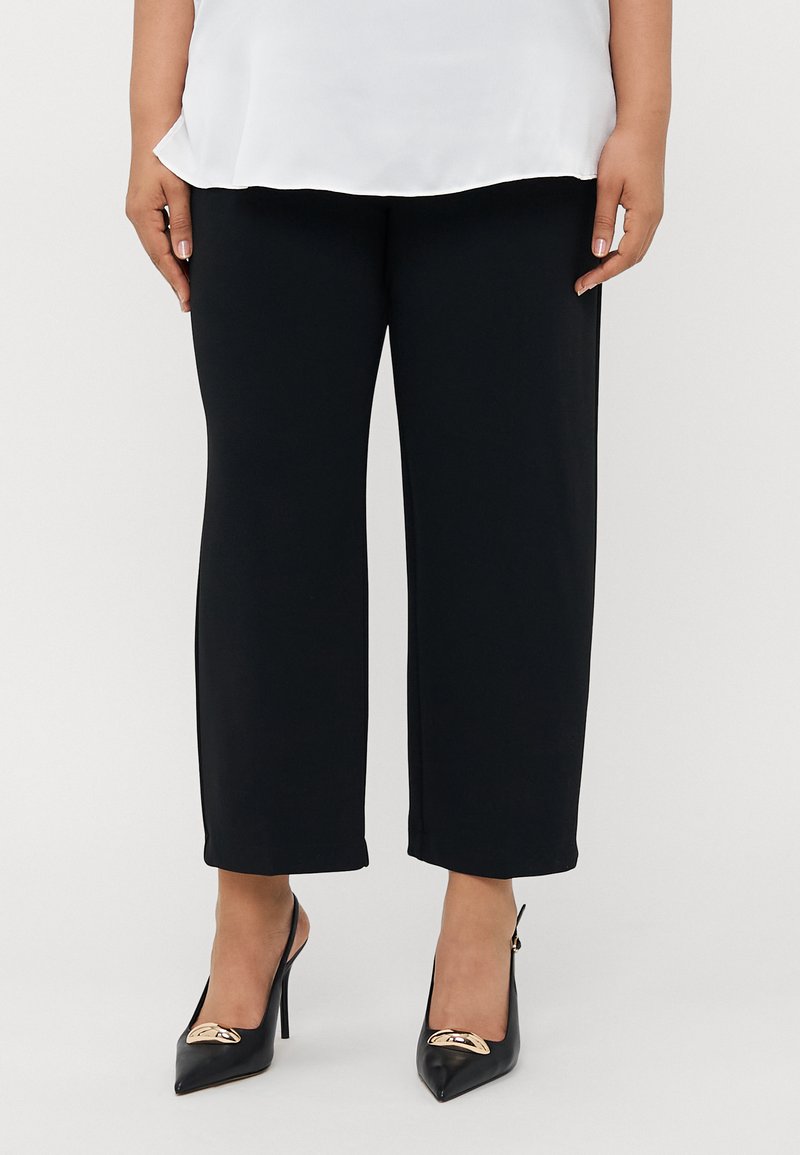 Black wide-leg pants made of a smooth fabric, paired with black high-heeled shoes featuring a gold accent on the toe.