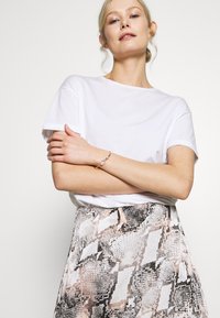 White cotton t-shirt with crew neck and short sleeves, paired with a patterned skirt featuring pink, black, and white geometric designs.