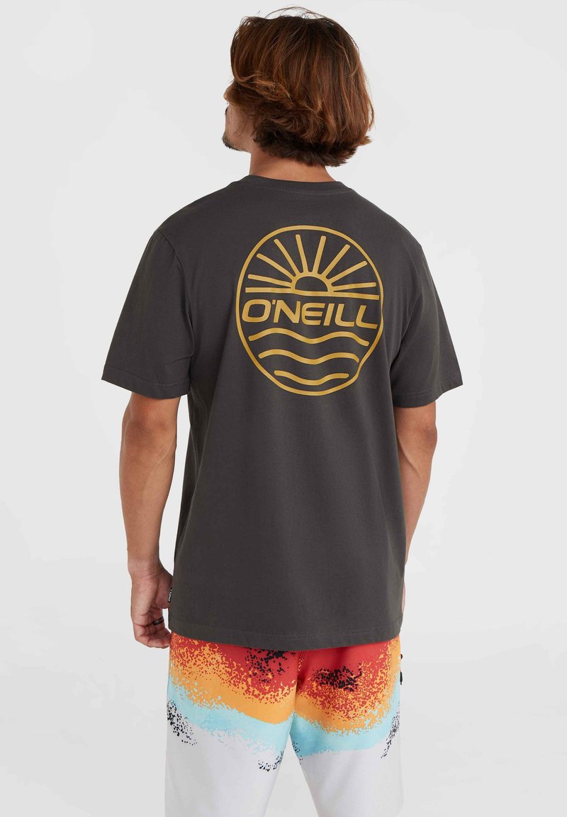 Camiseta gris oscuro con un gran logo de sol dorado y ola en la parte posterior, combinada con shorts de degradado colorido que presentan patrones en rojo, naranja y azul.