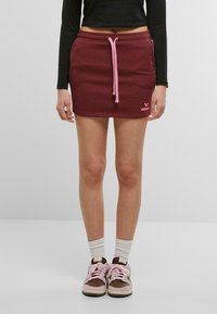 Bordový sweatshirt sukňa s ružovým �šnurovaním, so bočnými vreckami a malým logom. Komplementovaná hnedými a ružovými teniskami a bielymi ponožkami.