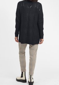 Svart stickad tröja med ett texturerat mönster, långa ärmar och design med sänkt axel, kombinerad med rutiga byxor och chunky svarta stövlar.