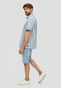Korte mouwen geruite blouse in lichtblauw en wit, gecombineerd met lichtdenim shorts en witte sneakers. Heeft een relaxte pasvorm en een kraag.