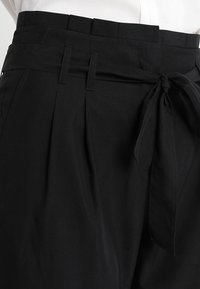 Zwarte tailleurbroek met een hoge tailleband, plooien en een strikband van stof. Gemaakt van gladde stof met een subtiele glans.