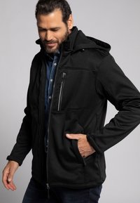 Schwarze Zip-Jacke mit Kapuze, aus weichem, strukturiertem Stoff. Verfügt über eine mit Reißverschluss gesicherte Brusttasche und zwei seitliche Handtaschen.
