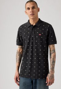 Musta polo paita, jossa on kuvio pieniä neliöitä kerma- ja vihreissä sävyissä, kauluksella ja punaisella Levi's-logoilla rinnassa.