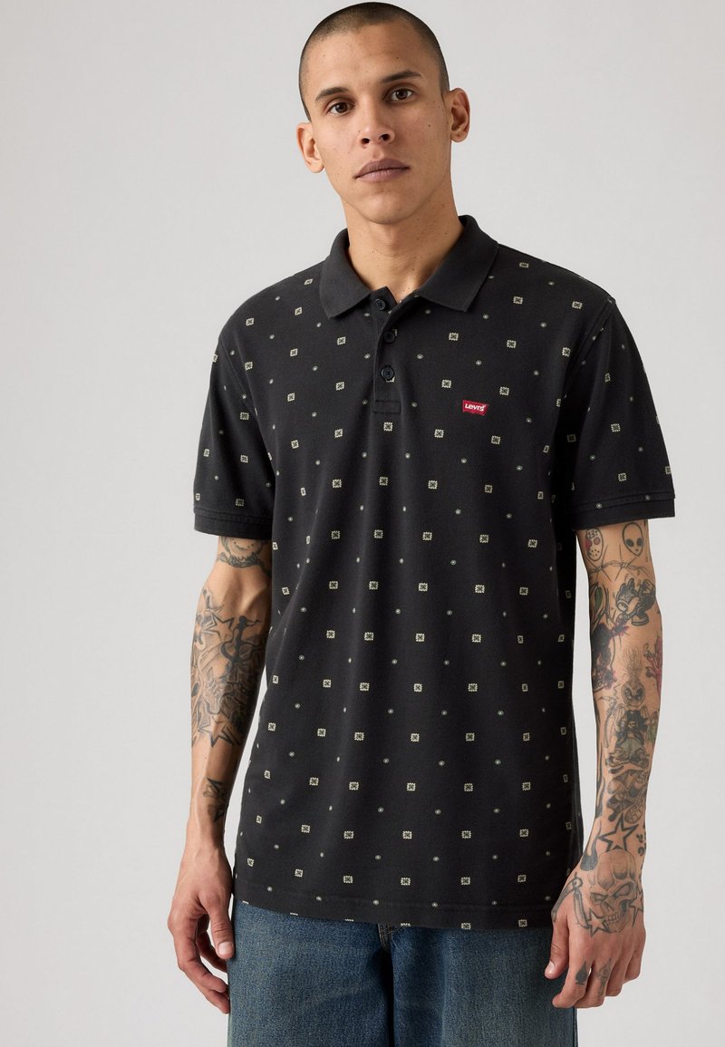 Musta polo paita, jossa on kuvio pieniä neliöitä kerma- ja vihreissä sävyissä, kauluksella ja punaisella Levi's-logoilla rinnassa.
