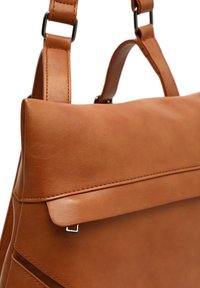 Mochila de cuero marrón con correas ajustables, solapa frontal y un pequeño detalle de hebilla plateada.