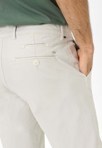 Pantaloni in cotone beige con due tasche posteriori con chiusura a bottone e una finitura testurizzata. La cintura presenta un piccolo dettaglio con logo.