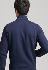 Felpa navy con colletto alto, polsini e orlo a coste. Realizzata in tessuto morbido, presenta una texture liscia e un design semplice e pulito.