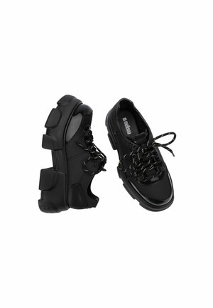 Coppia di sneaker nere chunky con suole spesse e testurizzate e lacci neri su sfondo bianco.