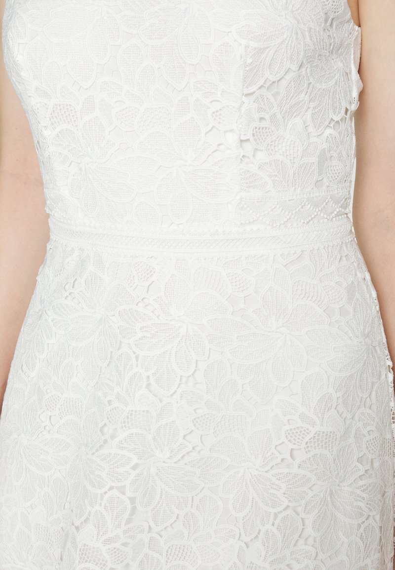 Vestido blanco de encaje con patrones florales, tejido texturizado, un cuerpo ajustado y un detalle en la cintura. La vista en primer plano muestra un intrincado trabajo de encaje.