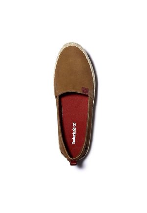 Bruine instapschoen met een suède bovenwerk, rood textielen binnenzool en een lichtgekleurde rubberen zool met structuur. Timberland-logo zichtbaar.