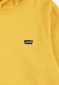 Gul bomullssweatshirt med et lite svart Levi's-logo-patch på brystet; glatt tekstur med et klassisk pullover-design.