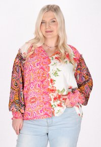 Blusa multicolore con motivi floreali e paisley, maniche lunghe a palloncino, chiusura a bottoni e tessuti misti nelle tonalità di rosa e bianco.