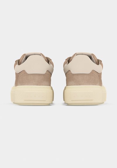 Ζευγάρι μπεζ σουέντ αθλητικά παπούτσια με ελαφρώς κρεμ φτέρνες και χοντρές εκρού υφασμάτινες σόλες, στερεωμένα από πίσω σε λευκό φόντο.