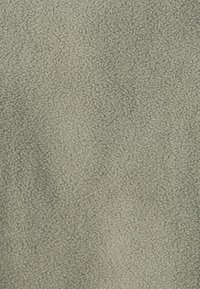 Blødt, lysegrønt stof med en tekstureret overflade, der har små, hævede fibre, som skaber en blød og hyggelig fornemmelse.