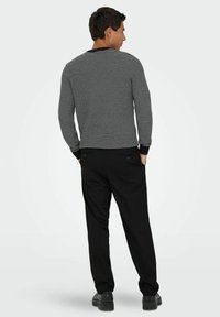 Schwarzes und weißes gemustertes Langarmhemd mit rundem Ausschnitt und schwarzen Bündchen, kombiniert mit schwarzen Hosen und dunklen Schuhen.
