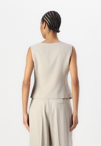 Svijetlo siva bezrukavna majica sa strukturiranim dizajnom, glatkom teksturom i blagim peplum detaljem, prikazana sa stražnje strane. Prilagođeni rez.
