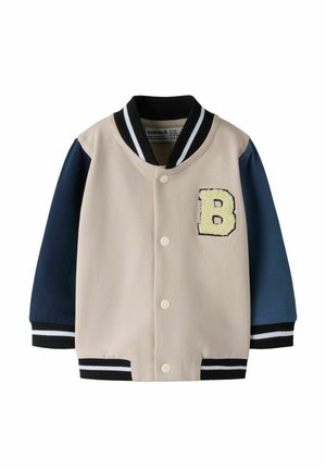 Børns beige og marineblå varsityjakke med sorte og hvide stribede manchetter og krave, trykknapper og et gult bogstav B-patch på brystet.