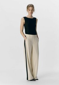 Top a costine nero abbinato a pantaloni wide-leg beige chiaro con una striscia laterale nera e tasche. Tacchi a punta nera.