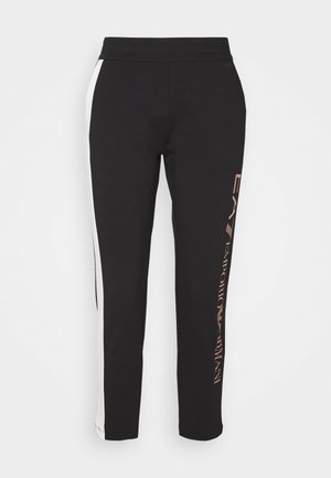Pantalon noir slim avec bandes blanches sur les côtés et logo "EA7 Emporio Armani" imprimé verticalement sur la jambe droite.