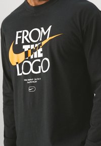 Black long-sleeve T-shirt featuring bold white and orange text "FROM THE LOGO" and Nike's logo, made from soft fabric with a smooth texture.