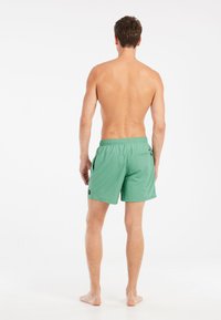 Shorts de bain verts en tissu texturé, avec taille élastique, poches latérales et poche arrière avec un petit logo.
