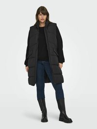 Svart pufferväst med hög krage och dragkedja, bärs över en svart tröja. Kombinerad med jeans i denim och svarta knähöga stövlar.