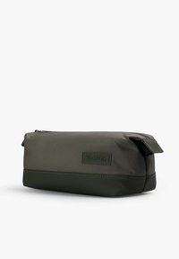 Bolsa de aseo rectangular en tela de verde oliva oscuro con una textura suave, que presenta una etiqueta de cuero y un cierre de cremallera en la parte superior.