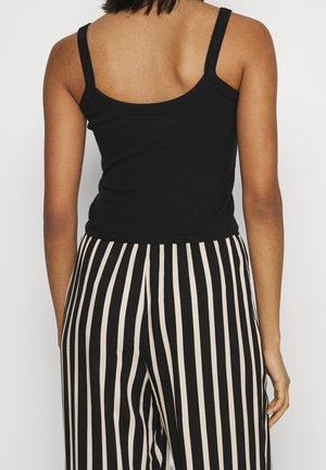 Black ribbed tank top with thin straps, paired with high-waisted black and beige vertical striped pants. Smooth, fitted texture throughout.