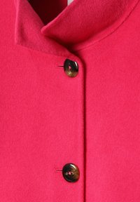 Manteau rose en feutre avec un col large, orné d'un bouton décoratif marron et de détails de couture contrastés le long de l'avant.