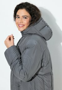 Graue Steppjacke mit Kapuze, versehen mit einem gesteppten Design und einem Reißverschluss. Glatte Textur und eine lässige Passform.