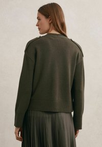 Maslinasto zeleni džemper s rebrastim rubom i manžetnama, s detaljima na ramenima. Stiliziran s plisiranom suknjom za slojeviti izgled.