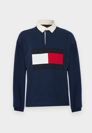 Polo de manga larga azul marino con cuello crema; presenta un gran parche de logo en rojo, blanco y azul marino en el centro; material de algodón.