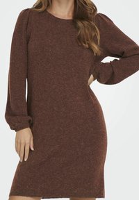 Abito maglione in un ricco marrone, con maniche lunghe a sbuffo e scollatura rotonda. Tessuto morbido con una linea dritta e leggera costina all'orlo.