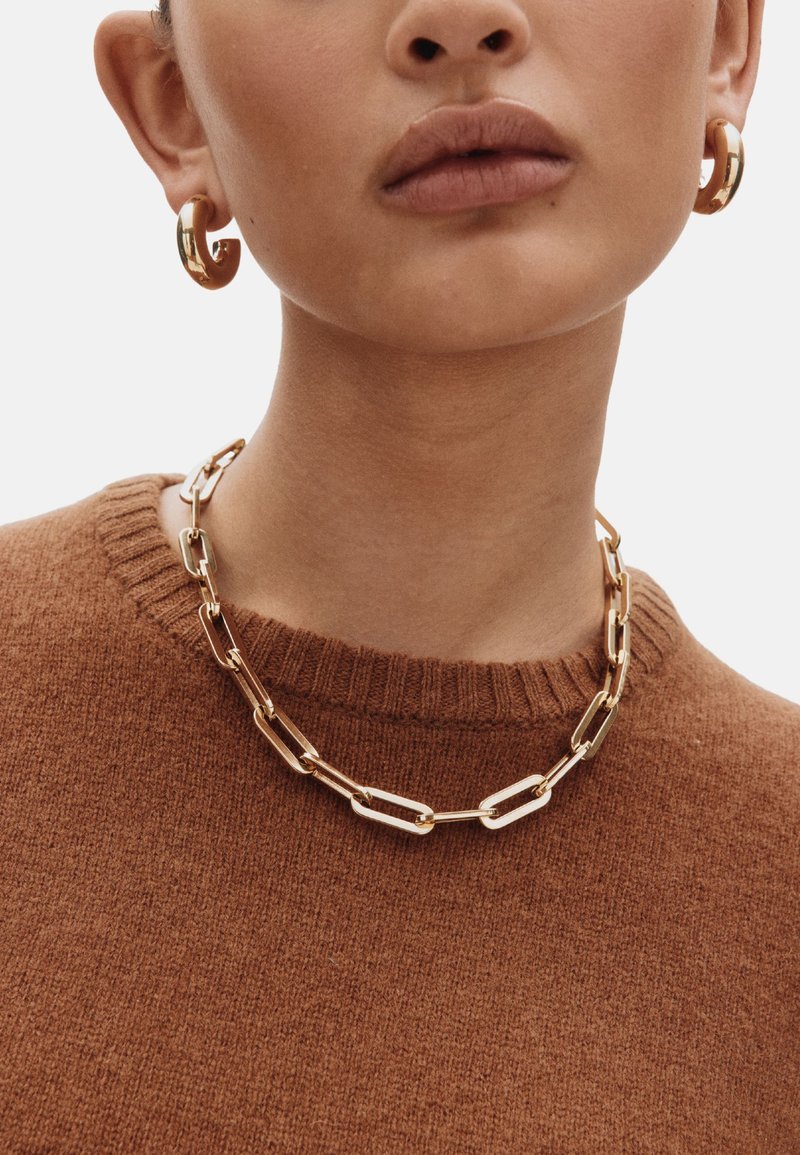 Kuldne ketiga kaelakee pika kujuga linkidega, kaaslaseks kuldsed rõngakujulised kõrvarõngad, kantud pruuni soonikkoega kampsuni peal, millel on soonikuga kaelus.