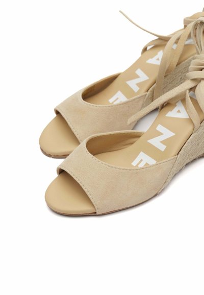 Sandali con tacco a cuneo in suede beige con design aperto, caratterizzati da una base in espadrille testurizzata e una suola beige, dettagliati con testo del logo bianco.