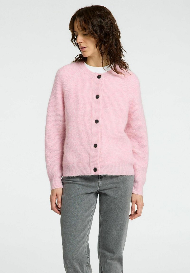 Cardigan rose en matériau doux et texturé, avec un col rond, des manches longues et six boutons noirs sur le devant.