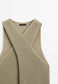 Beige knitted sleeveless top with a cross-over design. It features a textured, breathable fabric and a rounded neckline. Tag visible.