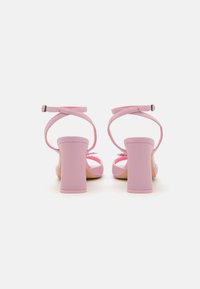 Sandales à talons roses avec une finition lisse et brillante. Elles possèdent des brides de cheville et un talon bloc épais. Le design est simple, sans motifs.