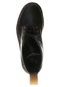 Botín de cuero negro hasta el tobillo con costuras amarillas, puntera redondeada y seis ojales. Cuenta con una lengüeta con "AirWair" en amarillo. Interior texturizado.