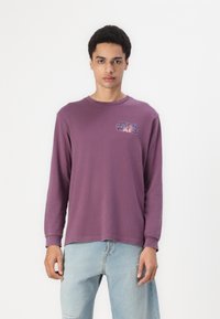 Long-sleeve purple cotton shirt with a round neck and a "Star Wars" logo on the chest. Paired with light blue distressed jeans.