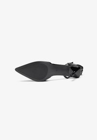 Chaussure noire à talon haut avec un design à bout pointu. Tige en cuir lisse avec une semelle texturée et un détail de bride à la cheville réglable.