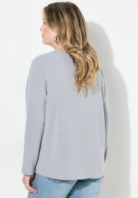 Lys grå langærmet top i blødt stof, med rund hals og diskrete syninger, parret med blå denim jeans.
